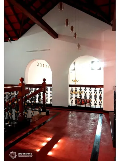 The first-floor corridor in the Udupi house, with its polished red oxide floor reflecting the light. Arched openings look down into the living area below, maintaining a visual connection between the two levels.