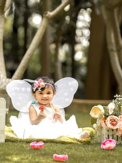 An enchanting outdoor butterfly-themed cake smash. The baby girl, dressed as a fairy with tiny wings, enjoys her first taste of cake in a beautiful garden setting, creating a magical and whimsical portrait.