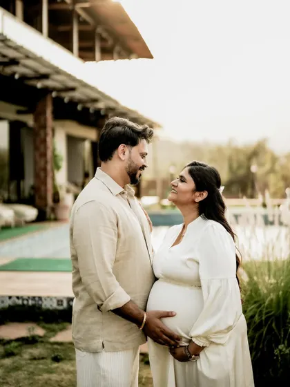 A beautiful indoor portrait near a pool. The couple looks at each other with love, their hands gently resting on the baby bump.