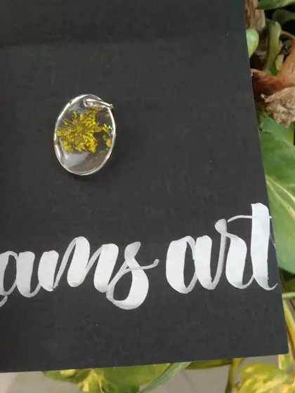 A close up of a small oval pendant with a tiny yellow flower inside, presented on my custom 'Lams art' card.