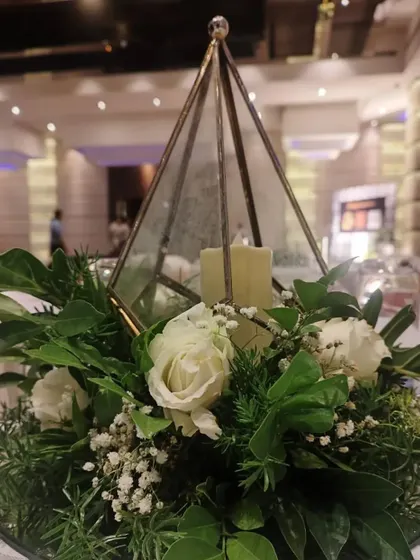 This elegant centerpiece was designed for a corporate dinner. A glass terrarium with candles is surrounded by a lush arrangement of white roses and fresh greenery, creating a sophisticated look.
