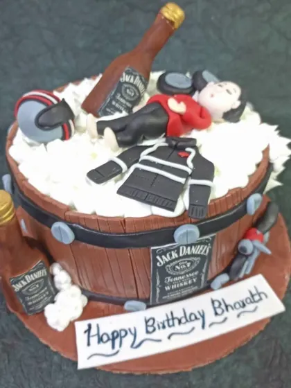 A fun and detailed cake for a Jack Daniel's and bike lover. The design features a barrel, miniature bottles, and a fondant figure passed out on top.