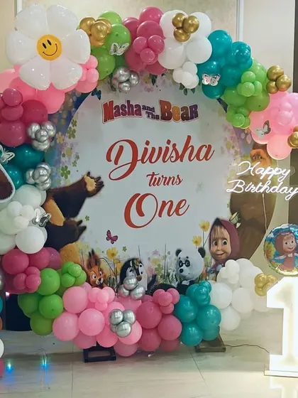 A sweet Masha and the Bear theme for a first birthday. This setup features a circular backdrop with character prints, a colorful balloon garland, and a light-up number '1' for a charming celebration.