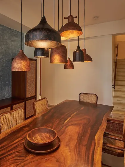 The dining area in the Magnolia Residence features a live-edge wooden table and custom-hammered copper pendant lights. The space is grounded by a blue accent wall, creating an intimate atmosphere for family gatherings.