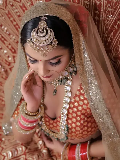 An elegant high-angle shot of the bride looking down. This pose highlights the intricate design of her maang tikka and the beautiful details of her dupatta.