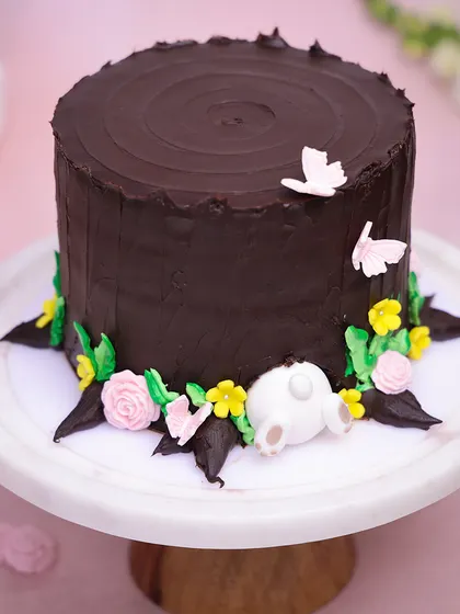 We create a whimsical woodland scene with this Easter burrow cake. A rich chocolate "tree trunk" is decorated with spring flowers, while a playful bunny is seen diving into the base, adding a touch of storybook magic to your holiday.
