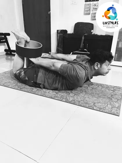 Using a yoga wheel to assist with Dhanurasana (Bow Pose). This prop helps to open the chest and shoulders more deeply while supporting the back, allowing for a more restorative stretch.