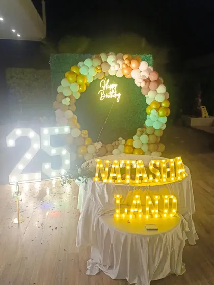 A glamorous outdoor 25th birthday party for "Natasha Land," with a balloon ring, green hedge backdrop, and light-up name and number displays.