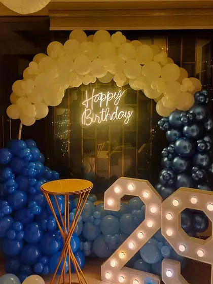 A close-up of a 29th birthday decoration, showing the blue and white balloon arrangement, neon sign, and light-up numbers.