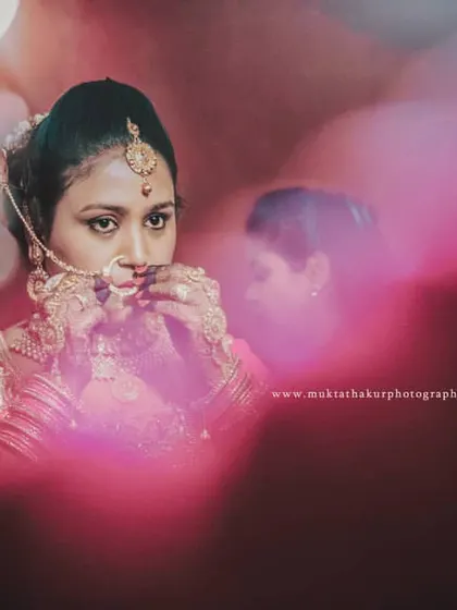 An artistic and moody shot of the bride adjusting her nath (nose ring), a key part of her traditional bridal look.