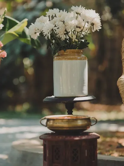A rustic and aesthetic decor detail, with white flowers in a traditional jar placed on vintage-style furniture.