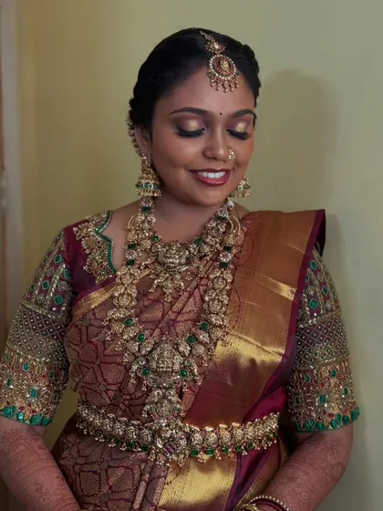 A smiling portrait of Prithivi, showcasing her complete Muhurtham look. The gold and green tones in her jewellery and saree are complemented by a warm, glowing makeup application.