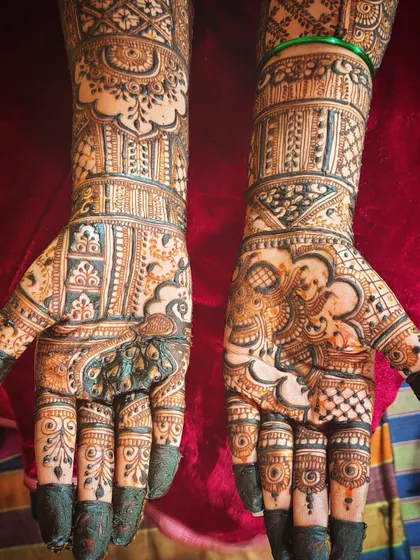This bridal mehendi showcases a mix of bold and fine work. The peacock on the left hand is filled with delicate details, contrasting with the strong lines of the architectural patterns on the right.
