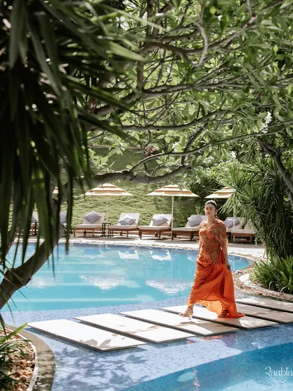 A beautiful shot of the bride walking by the pool, her orange dress a vibrant splash of color against the lush greenery and blue water.