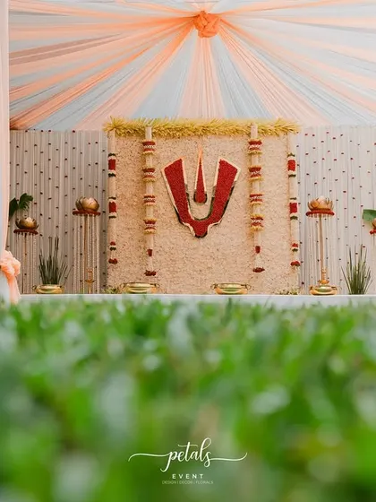 A low angle shot capturing the grandeur of the Telugu Nalugu mandap. The peach and white draped ceiling of the tent adds a soft, warm glow to the entire setup, enhancing the divine ambiance.