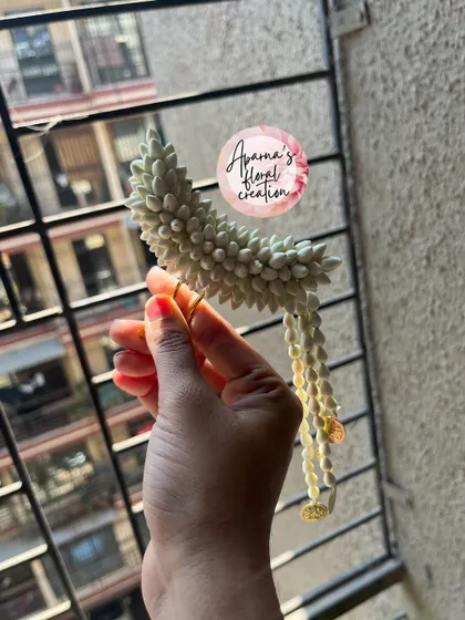 A 'Chandrakor' style hair pin, shaped like a crescent moon. This delicate accessory is made from jasmine buds and is a beautiful addition to a traditional hairstyle.