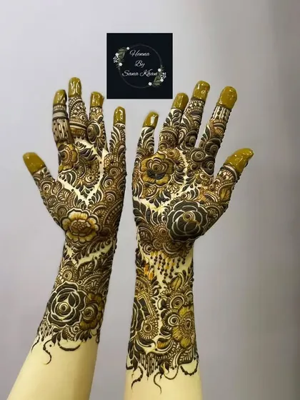 A full and festive floral design reaching up the wrists, with the henna paste still on, showing the clean and precise application.
