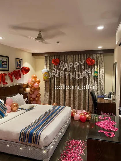 This image focuses on the "Happy Birthday" foil balloon setup against the curtains, part of a comprehensive hotel room surprise package.