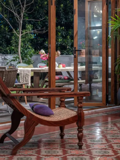 Looking from the inside out in the Dhaka home, this view captures the seamless connection between the interior and the garden. The patterned floor tiles lead the eye towards the outdoor dining area, framed by large wooden and glass doors that can be folded away.