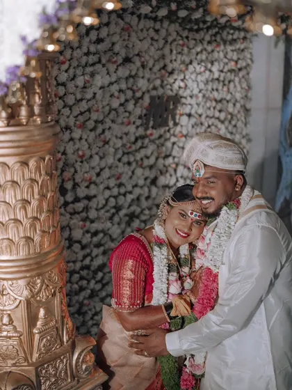 A happy embrace between the newly married couple against a wall of white flowers.