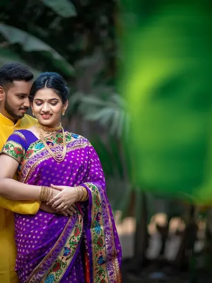 A tender embrace in a lush, green setting. The bride's vibrant purple Paithani saree adds a beautiful pop of color to this traditional portrait.