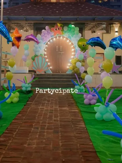 The walkway to the 'Under the Sea' party, with a green carpet 'seabed' and balloon sculptures mimicking coral and sea plants. The lit arch at the end draws guests forward.