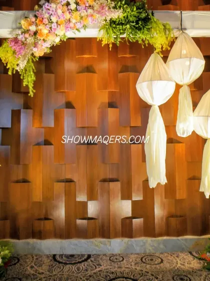 A unique photo booth with a textured wooden backdrop, framed by pastel florals and adorned with artistic fabric lanterns.
