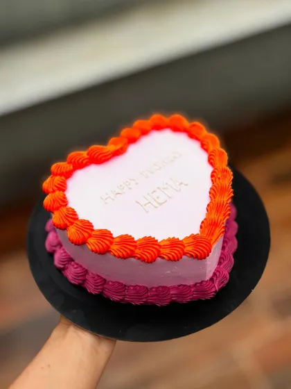 A simple and sweet heart-shaped birthday cake. The two-tone pink and orange buttercream border adds a vibrant touch.
