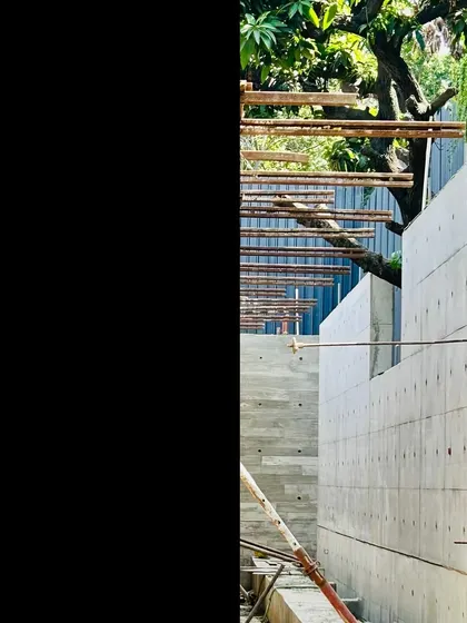 An exposed concrete wall under construction, with reinforcing bars extending from the top, ready for the next pour. The formwork tie-rod holes create a systematic pattern on the facade.