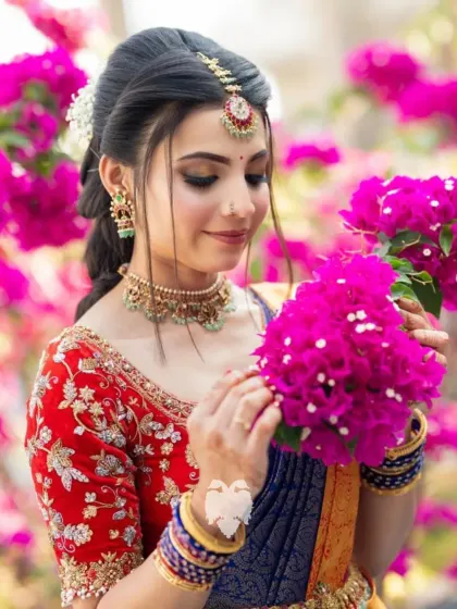Bride Jahnavi, surrounded by flowers, her red velvet pre-wedding blouse adding a pop of vibrant color.