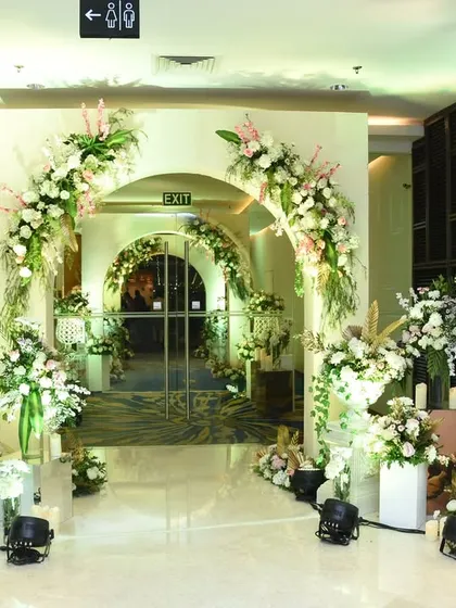 A series of elegant white floral arches creates a beautiful and grand hallway for guests to walk through. This design transforms a simple corridor into a memorable part of the event experience.