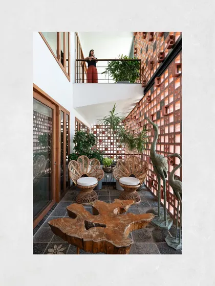 The alternating balconies at Kamala Residence create engaging visual connections between floors. This courtyard-like space is furnished with a live-edge table and peacock-style cane chairs, creating a private garden oasis.