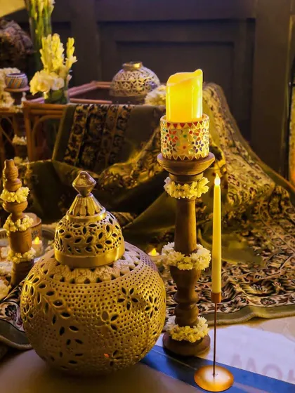 An intimate and regal setup featuring an ornate brass lantern and a candle holder adorned with jasmine. The rich, patterned fabrics in the background add a touch of royalty.