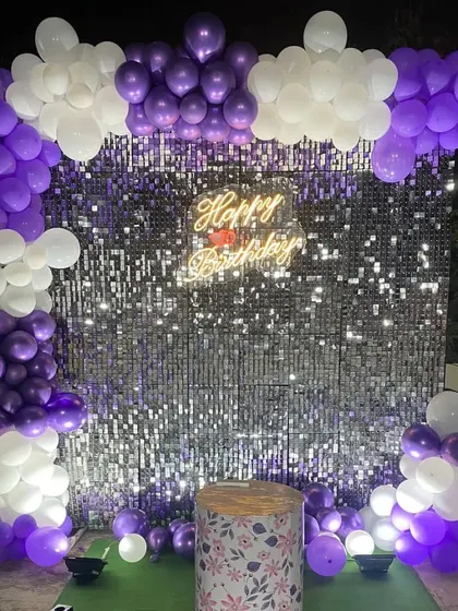 A purple and white balloon arch frames this silver shimmer wall, creating a vibrant and fun photo corner for a birthday celebration.