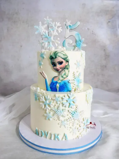 A grand two-tier Frozen cake for a 5th birthday. This design features a beautiful edible image of Elsa, surrounded by a flurry of intricate sugar snowflakes.
