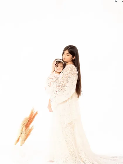 A mother holds her daughter close in a tender embrace. The soft, high-key lighting and their matching lace outfits create a delicate and angelic mother-daughter portrait.