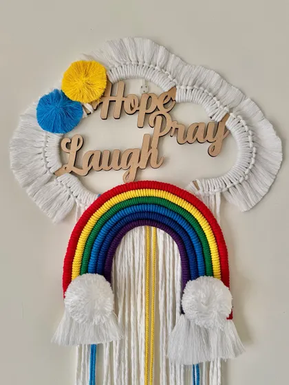A close-up of the custom phrase "Hope Pray Laugh" on this rainbow wall hanging.