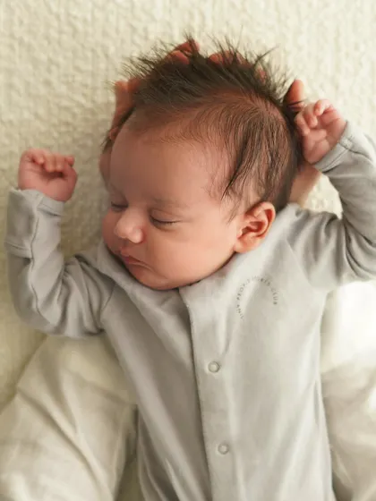 A close-up of a newborn's sleepy face and spiky hair, with their tiny fists raised. I love capturing these quirky and adorable details.