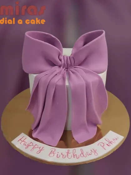 A simple yet stunning gift-box cake. The clean white cake is topped with a large, beautifully sculpted lavender bow, making the cake itself the present.