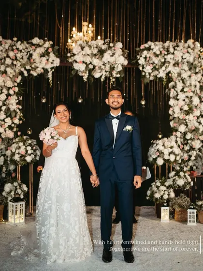 The newlyweds stand proudly under their floral wedding arch. This is the quintessential "just married" portrait, full of happiness and accomplishment.