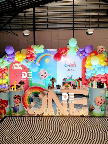 A cheerful Cocomelon first birthday for Darsh. This party features a rainbow balloon arch, multiple character cutouts, and a large 'ONE' table, creating a perfect setting for a memorable celebration.
