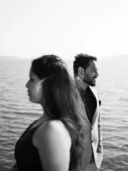 An artistic black and white shot of a couple by the sea, looking in opposite directions. This composition creates a modern, thoughtful mood for a pre-wedding portrait.