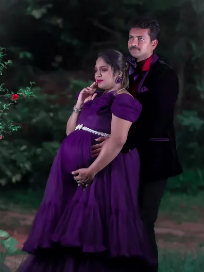 A romantic outdoor maternity photo of a couple, with the woman in a beautiful purple gown and the man in a classic black suit.