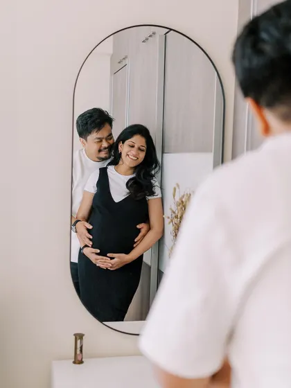 A creative reflection shot capturing the couple's embrace in the mirror. This perspective adds a layer of intimacy and artistry to the home maternity session, showing the moment from a different point of view.