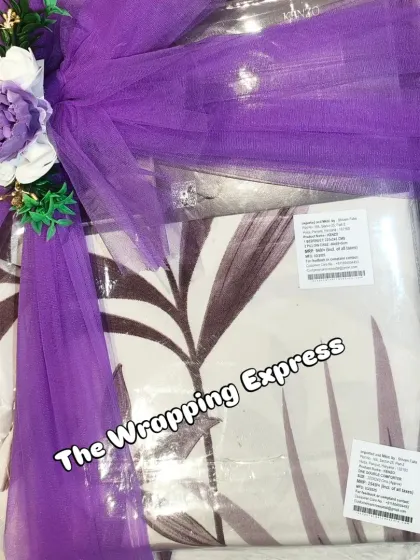 A bedding set for a baby girl, packed and decorated with a matching purple floral arrangement.