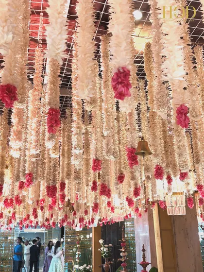 A beautiful shot of the floral canopy ceiling, with hanging bells and crystal chandeliers interspersed among the flowers. This combination of elements adds a touch of tradition and sparkle to the decor.
