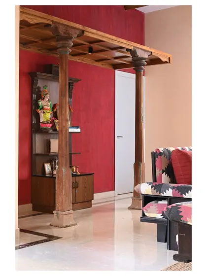 A family lounge with a deep-red accent wall and reclaimed Chettinad pillars, creating a cozy and traditional temple area.