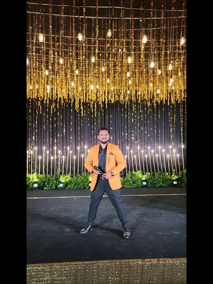 On stage in a sharp orange blazer, ready to light up the Sangeet night.