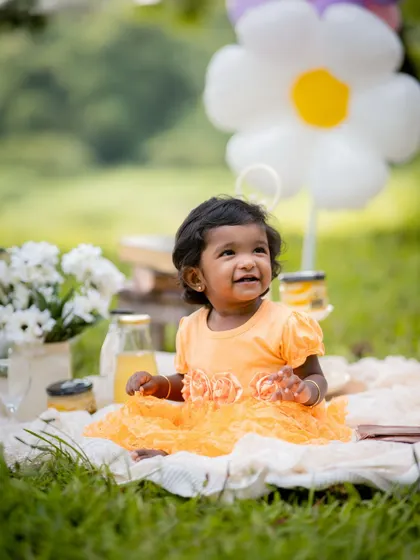 A sweet picnic in the park. The soft green grass and a simple setup with flowers and juice create a lovely, relaxed atmosphere for a baby photoshoot.