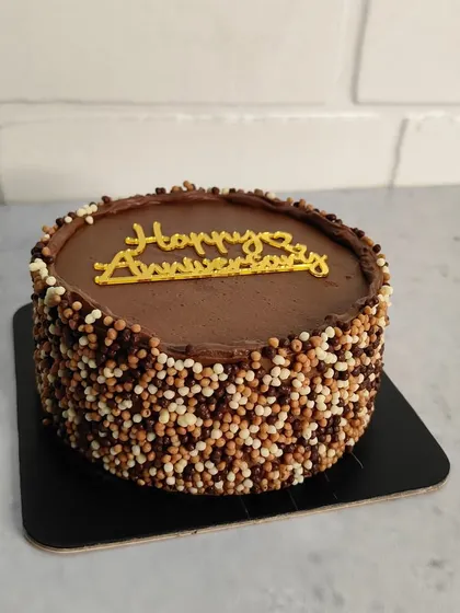 A classic chocolate anniversary cake. The sides are covered in crunchy chocolate crispies, and a simple "Happy Anniversary" message makes it a perfect, delicious way to celebrate.